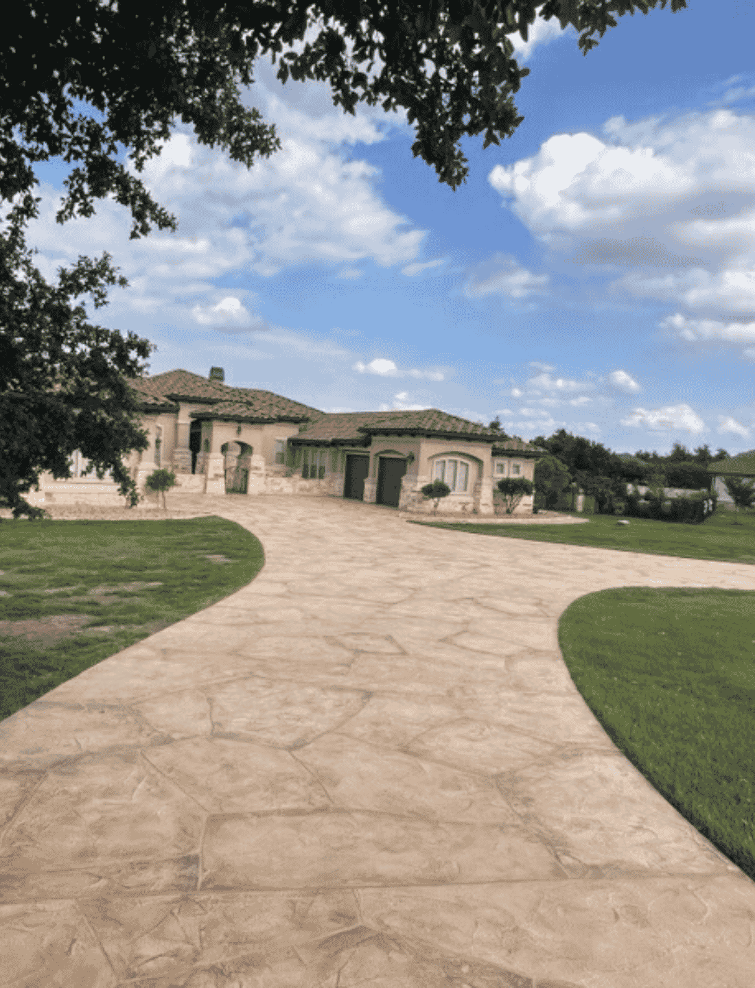 Austin TX Flagstone Beige with brown grout Flagstone-pattern concrete driveway leading to a stone and stucco home entrance.